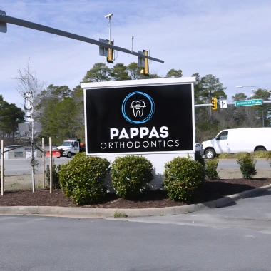 Pappas Orthodontics roadside sign with logo surrounded by landscaping, street view, and traffic lights.