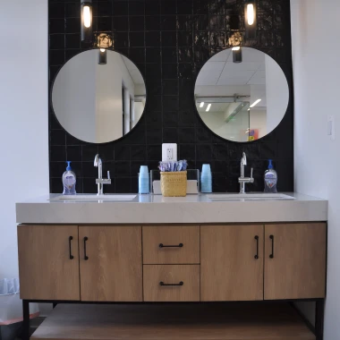 Modern double sink vanity with round mirrors and wooden cabinets at Pappas Orthodontics office.